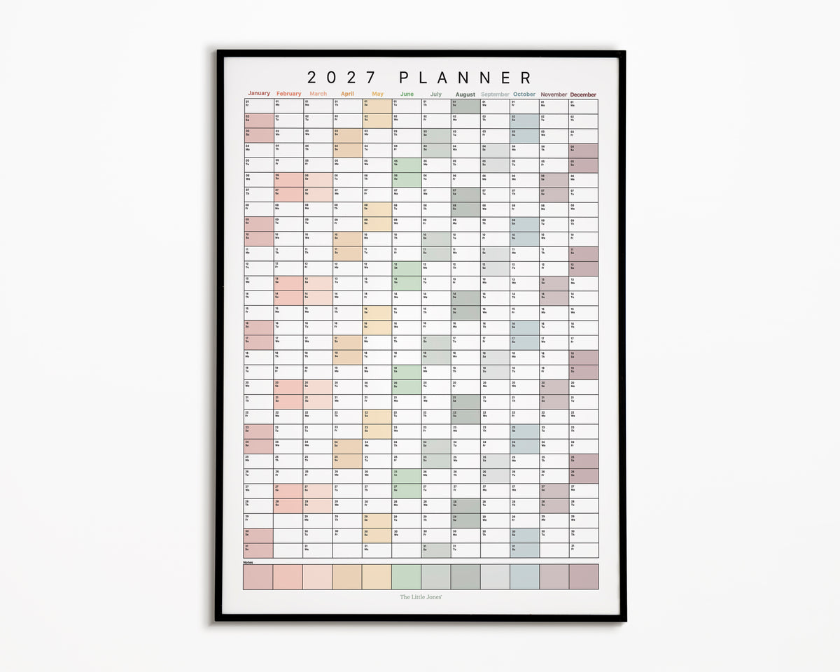 A framed 2027 annual wall planner for families with a minimalist monthly calendar grid in soft pastel colours, displayed against a whitebackground.