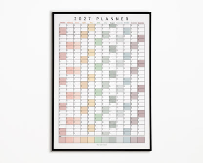 A framed 2027 annual wall planner for families with a minimalist monthly calendar grid in soft pastel colours, displayed against a whitebackground.
