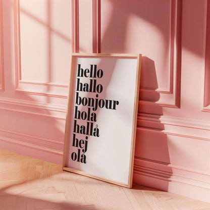 Framed poster with 'hello hallo bonjour hola hallá hej öla' text on a pink wall.