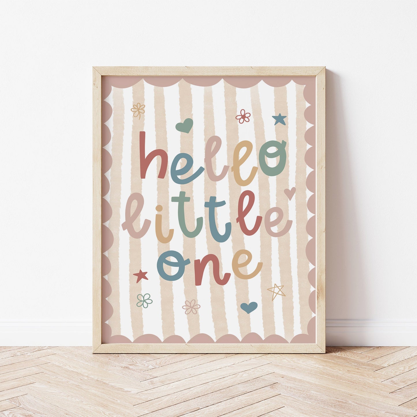 Framed artwork with 'hello little one' text on a striped background, placed on a wooden floor.