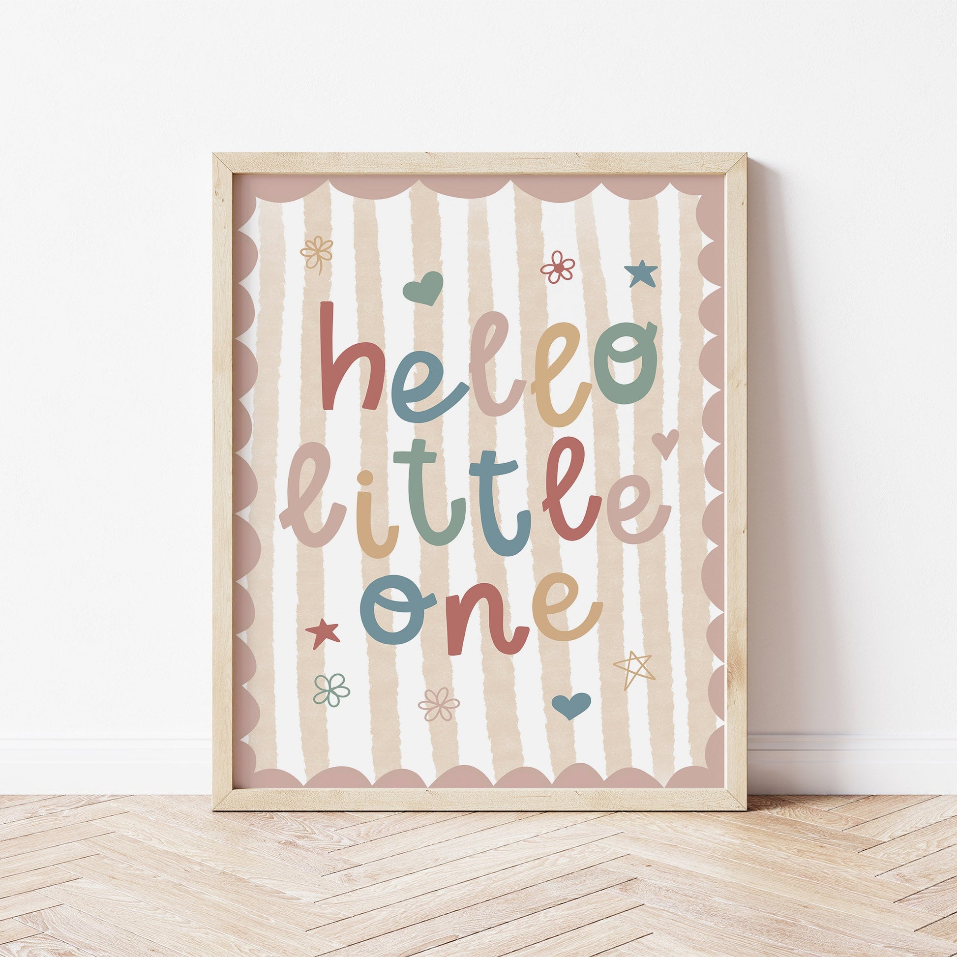 Framed artwork with 'hello little one' text on a striped background, placed on a wooden floor.
