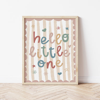 Framed artwork with 'hello little one' text on a striped background, placed on a wooden floor.
