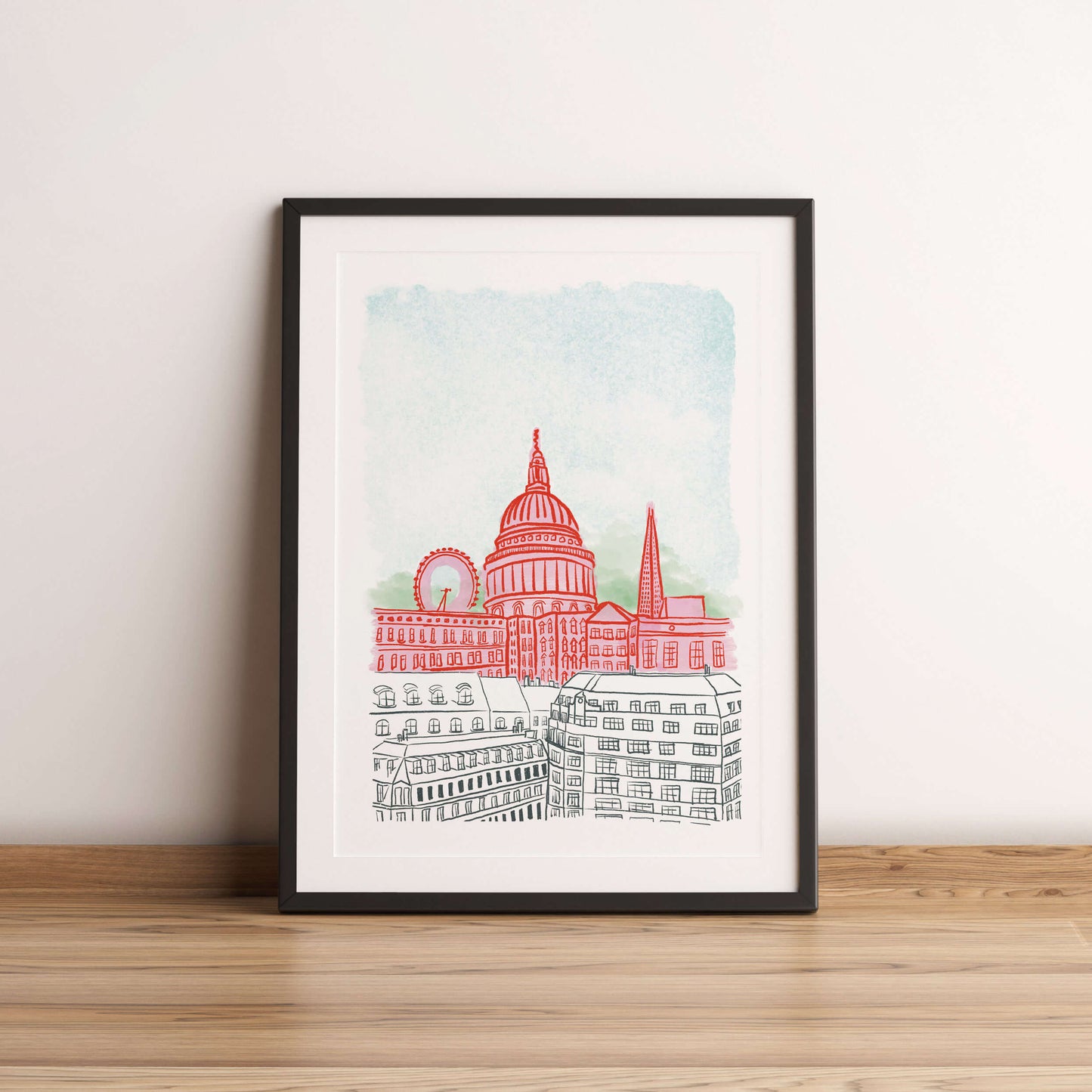 Framed artwork of a cityscape with a prominent building on a wooden floor against a white wall.