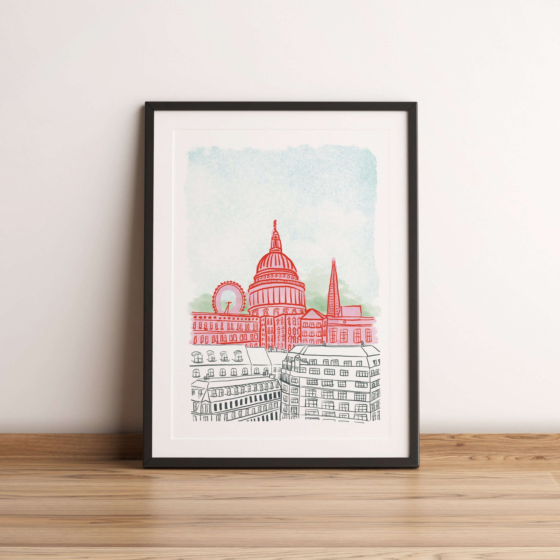 Framed artwork of a cityscape with a prominent building on a wooden floor against a white wall.