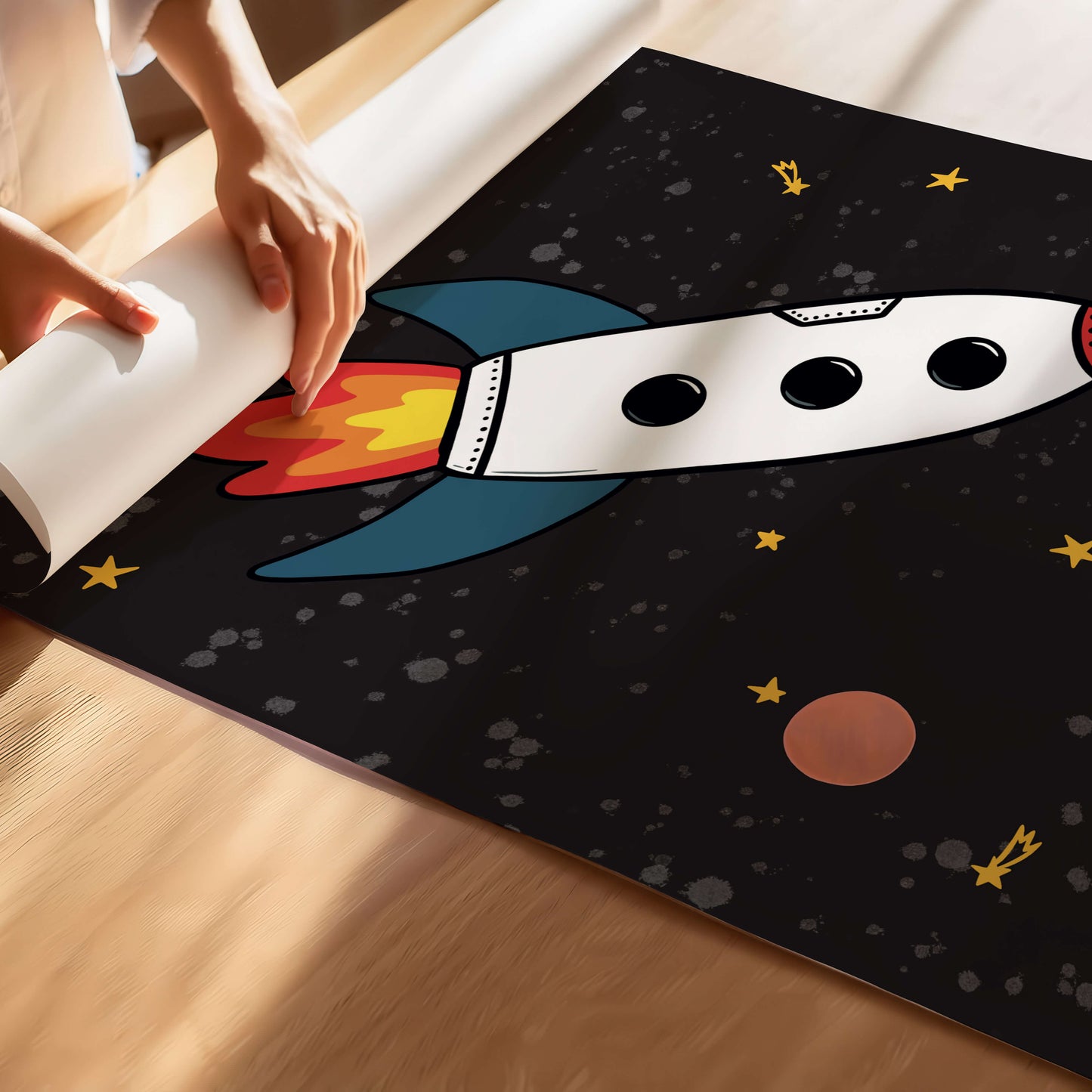 Person unrolling a space-themed kids' print with a rocket design.