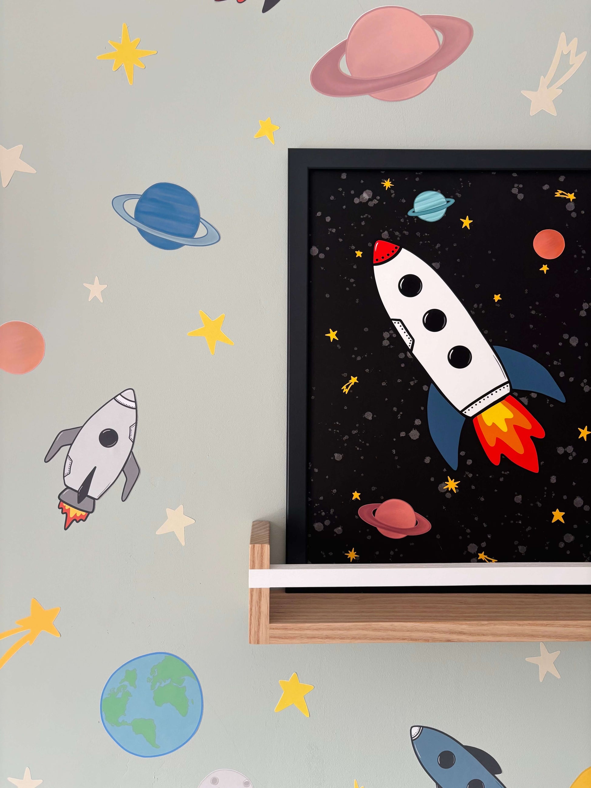 Framed artwork of a rocket ship on a wall with space-themed decorations.